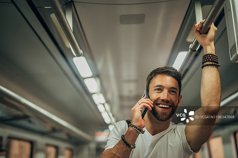 在地铁车厢里用手机交谈的男人图片素材