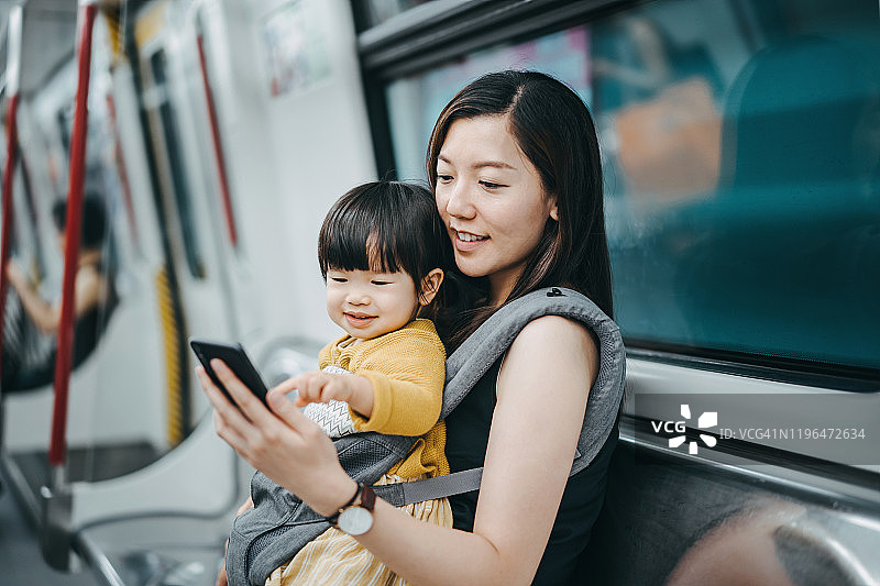 年轻的母亲和可爱女儿在地铁上快乐地使用智能手机图片素材