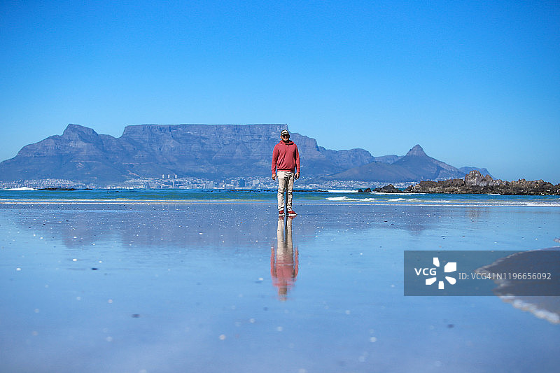 一名亚洲男子站在海滩上，背景是桌山图片素材