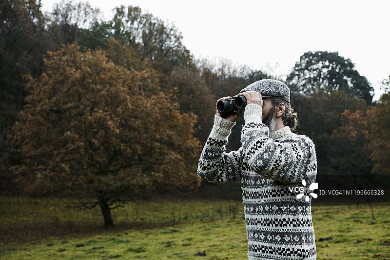 穿毛衣的男人在森林里用望远镜观察图片素材