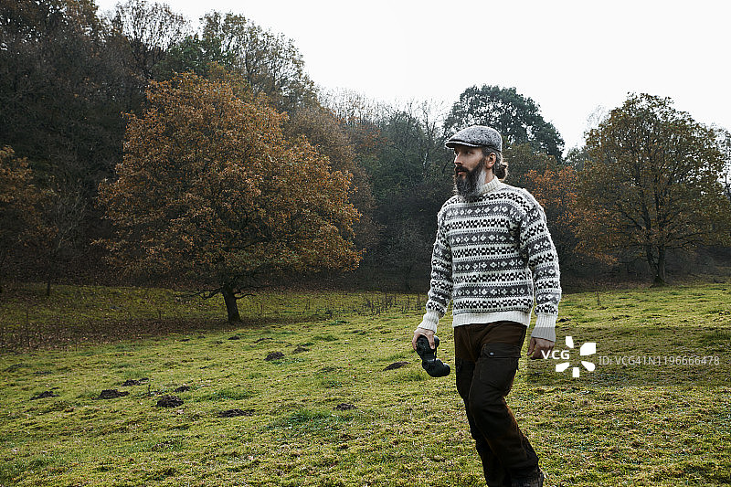 戴着毛衣和帽子，在田野里拿着双筒望远镜行走的男人图片素材