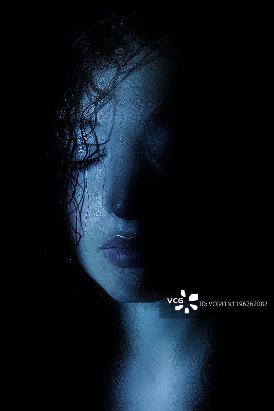 年轻女子闭着眼睛，湿漉漉的黑发，戏剧性的冷光照亮了半张脸图片素材