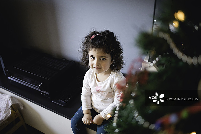 快乐的小女孩在圣诞树旁看着镜头图片素材