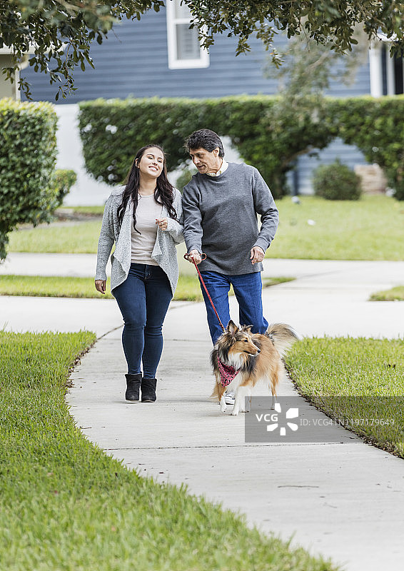 年长的西班牙裔男人和成年女儿在遛狗图片素材