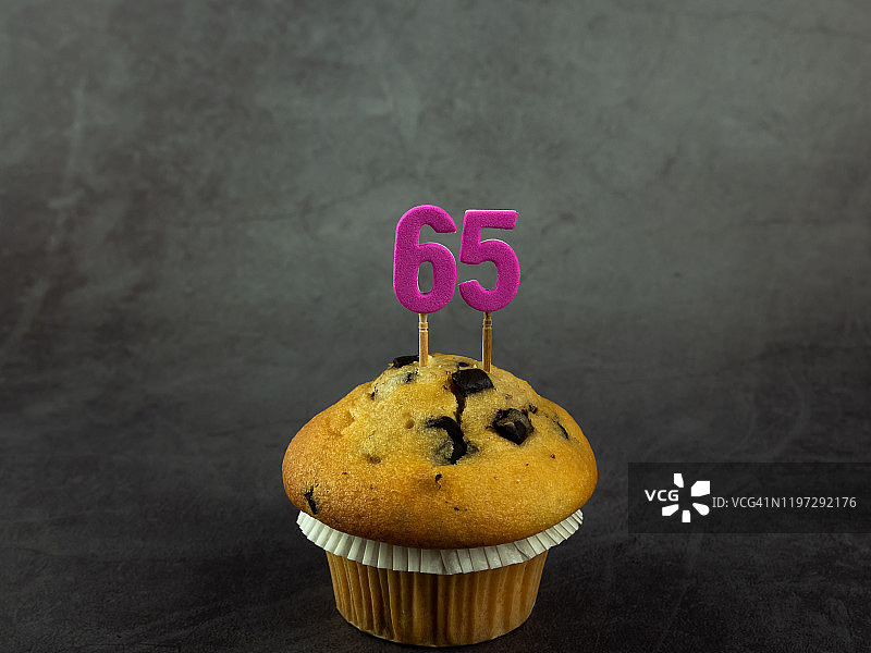 65岁生日纸杯蛋糕蜡烛，深色背景巧克力碎片图片素材