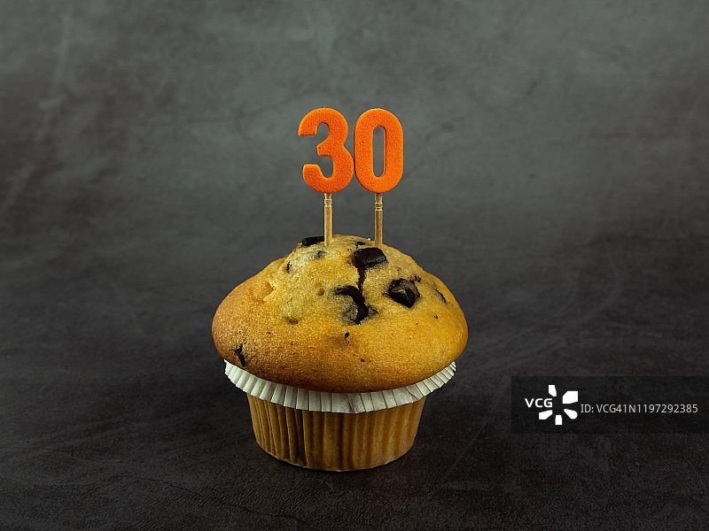 深色背景下带有巧克力片的纸杯蛋糕上的30岁生日蜡烛图片素材