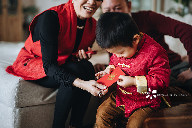 穿着红色中国传统服装的可爱小孙子双手从祖父母那里高兴地接过新年红包图片素材