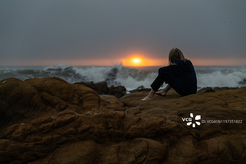 青少年坐在岩石岸边眺望日落海景图片素材