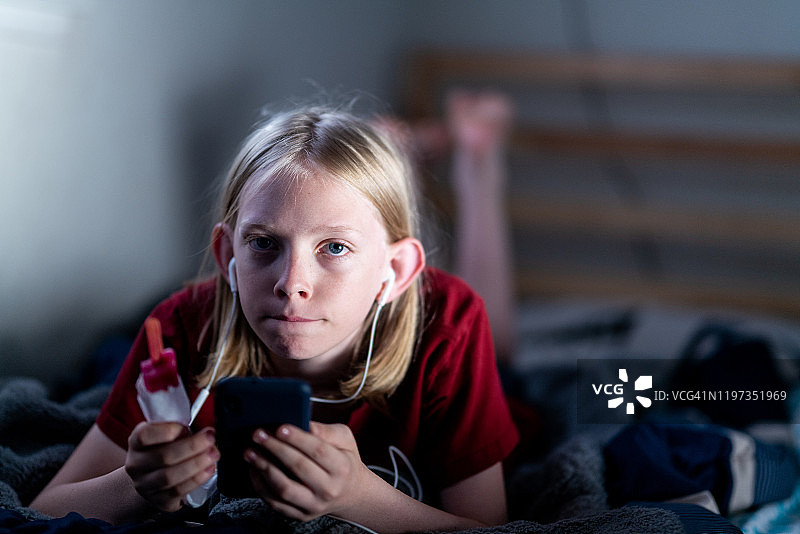拿着冰棒躺在床上，玩手机、戴着耳机的少年图片素材