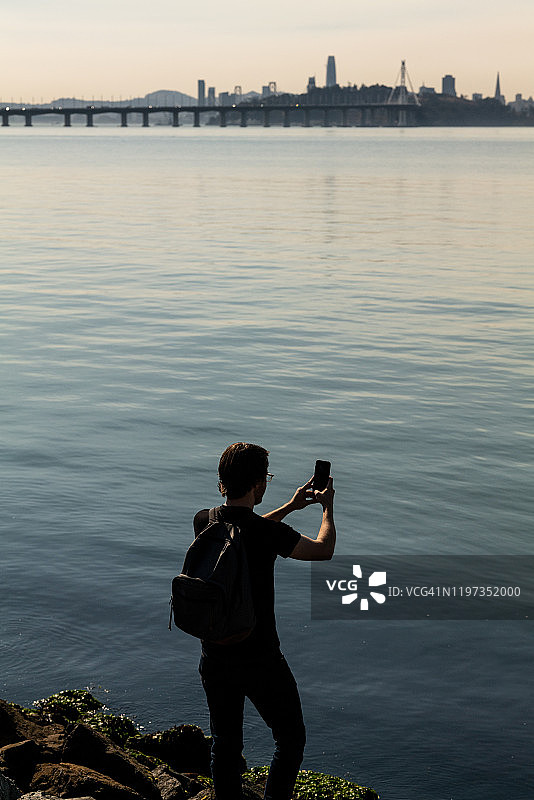 男人站在岩石岸边用手机拍摄旧金山图片素材
