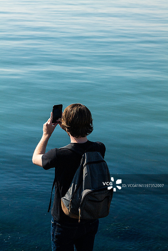 男人站在海湾边用手机拍照图片素材