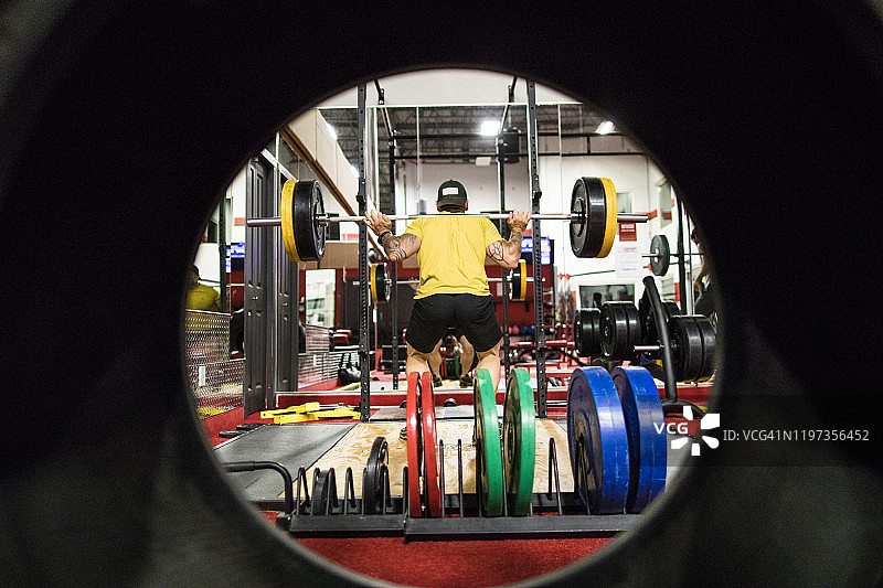 透过轮胎看在健身房做深蹲的健壮男人图片素材