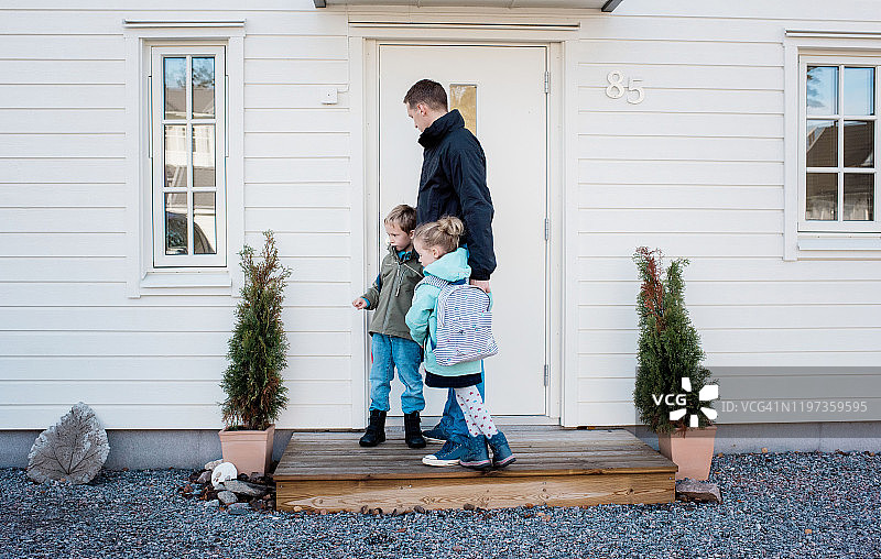 父亲送孩子上学后锁上前门图片素材