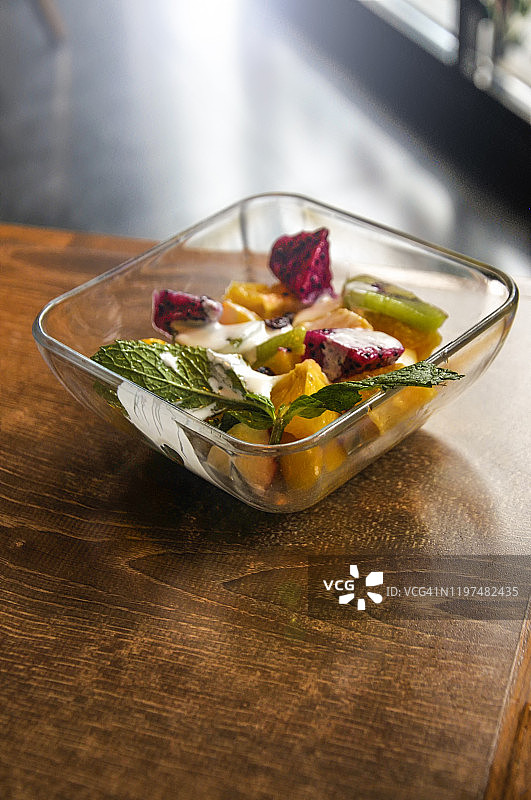 木桌上玻璃碗中盛放的芒果、火龙果混合沙拉叶图片素材