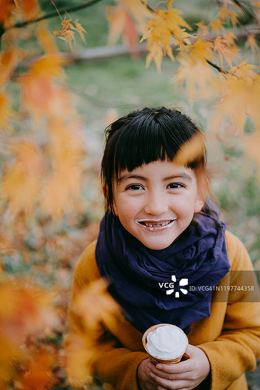 东京秋叶下，手拿冰淇淋对着镜头微笑的可爱学龄前女孩图片素材