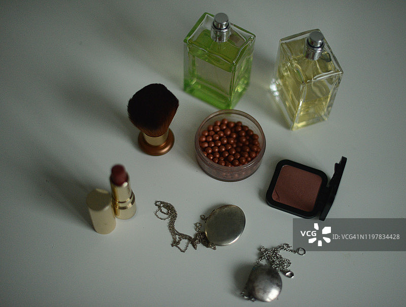 两瓶香水、红色唇膏和一罐古铜色珍珠在白色背景上图片素材
