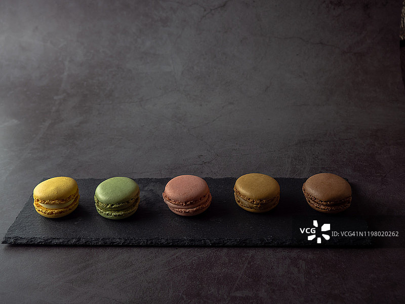 深灰色背景下石板盘中的一排马卡龙图片素材