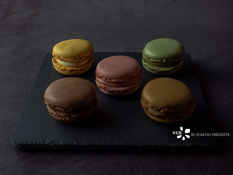 深灰色背景下的石板盘上的几个马卡龙图片素材