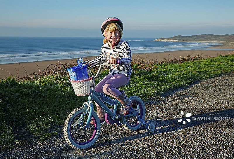 4-5岁女孩骑着带辅助轮的自行车，眺望海滩图片素材