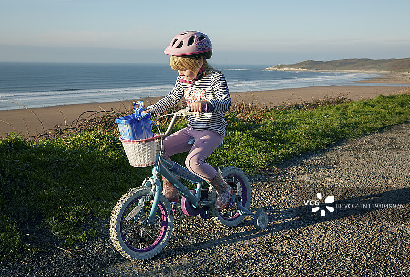 4-5岁女孩骑着带辅助轮的自行车，眺望海滩图片素材