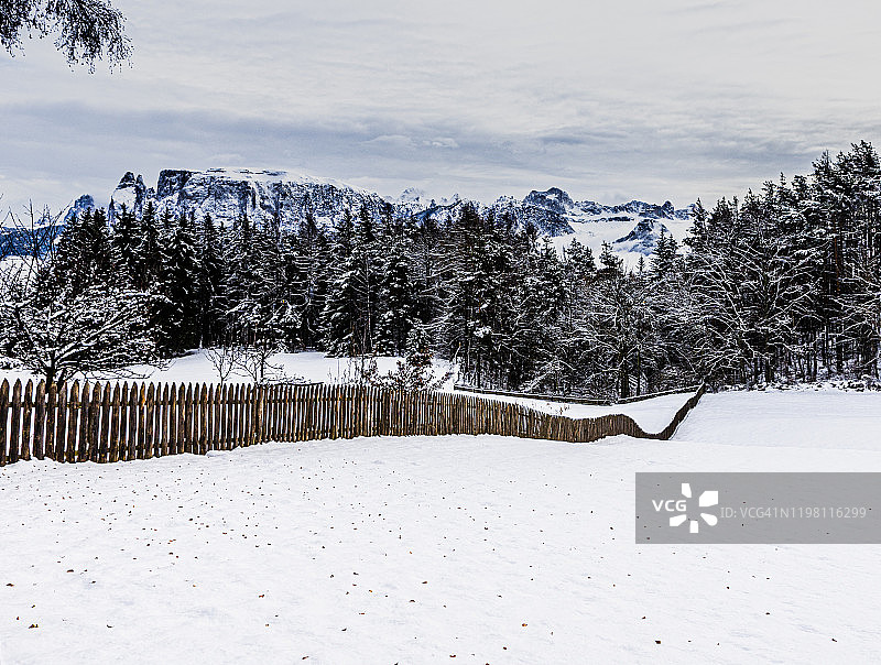 被雪覆盖的土地上的长长的栅栏。多洛米蒂山脉在后面。图片素材