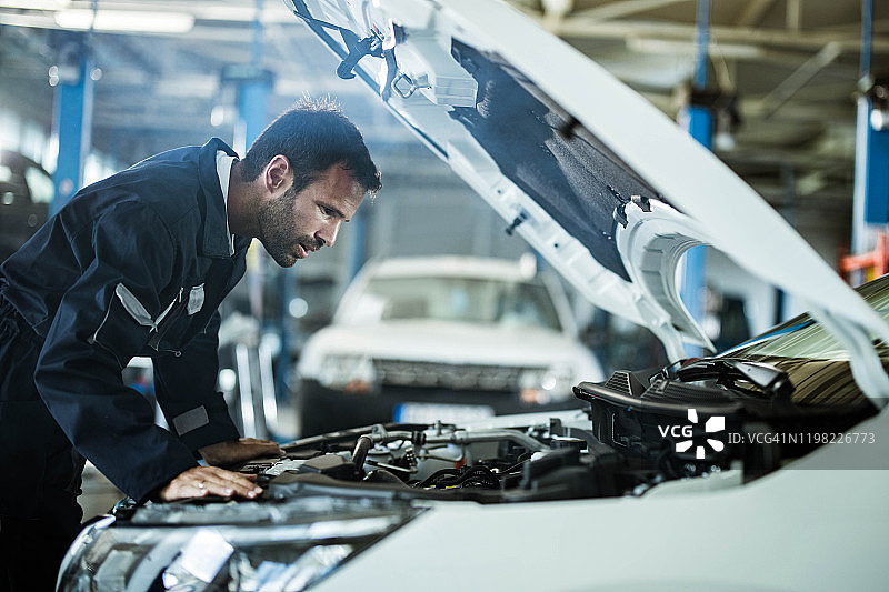年轻的修理工在汽车修理店检查发动机问题图片素材