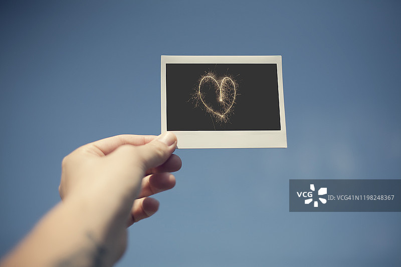 蓝天下的手拿着带有心形图案的宝丽来照片图片素材