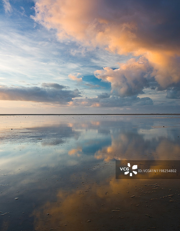 竖版照片：日落时分海滩上云彩的对称倒影图片素材