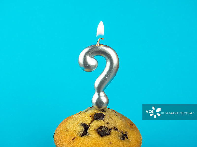纸杯蛋糕上的问号生日蜡烛，蓝色背景上带有巧克力片图片素材