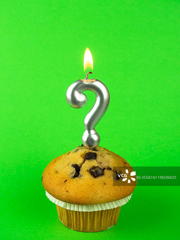 绿色背景上带有巧克力片的纸杯蛋糕上的问号生日蜡烛图片素材