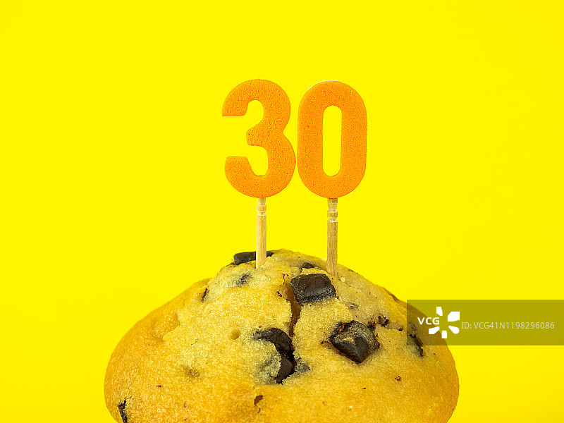黄色背景上带有巧克力片的纸杯蛋糕中的30岁生日蜡烛图片素材