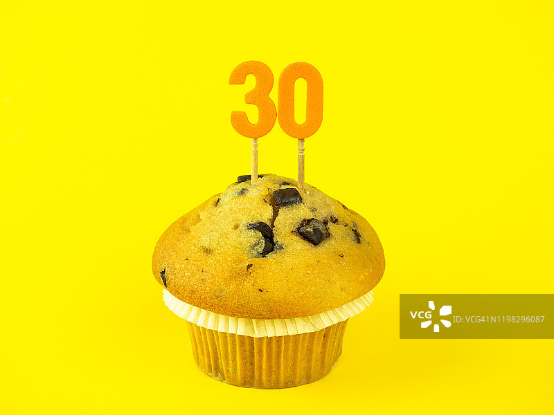 黄色背景上带有巧克力片的纸杯蛋糕中的30岁生日蜡烛图片素材