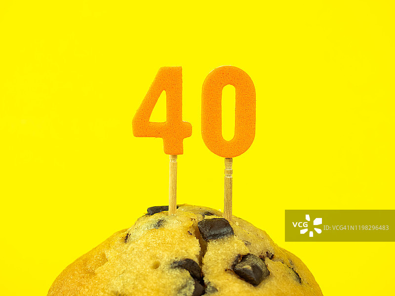 黄色背景上带有巧克力碎片的纸杯蛋糕上的40岁生日蜡烛图片素材