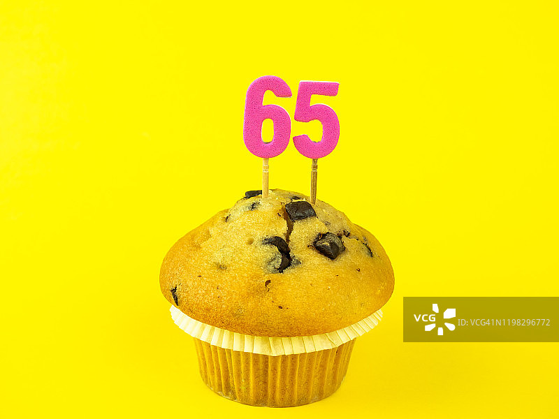 纸杯蛋糕上的65岁生日蜡烛，配巧克力碎屑黄色背景图片素材