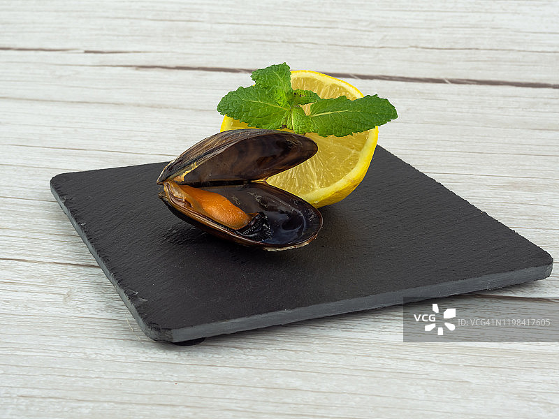 石板盘上放着打开的贻贝和半个柠檬与薄荷叶图片素材