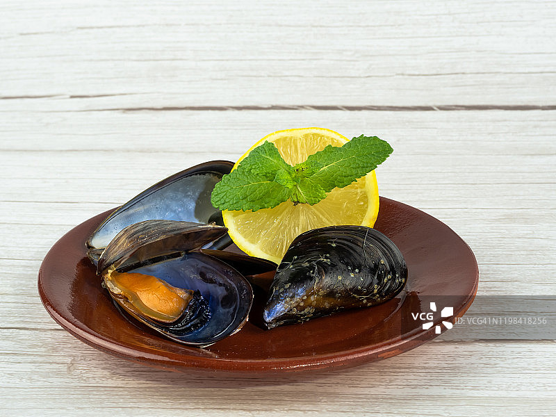 黏土盘子上打开的贻贝和贻贝壳以及半个柠檬与薄荷叶图片素材