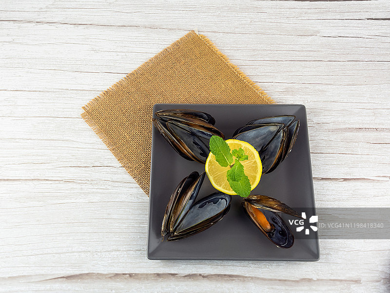 粗麻布上方形盘子里放着打开的贻贝、贻贝壳、半个柠檬和薄荷叶图片素材