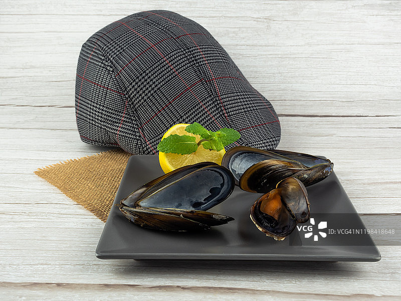 打开贻贝，贻贝壳和半个柠檬，一些薄荷叶放在粗麻布上的方盘中和一个遮阳帽图片素材