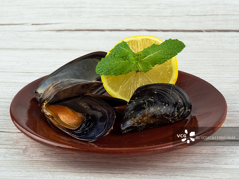 黏土盘子上打开的贻贝和贻贝壳以及半个柠檬与薄荷叶图片素材