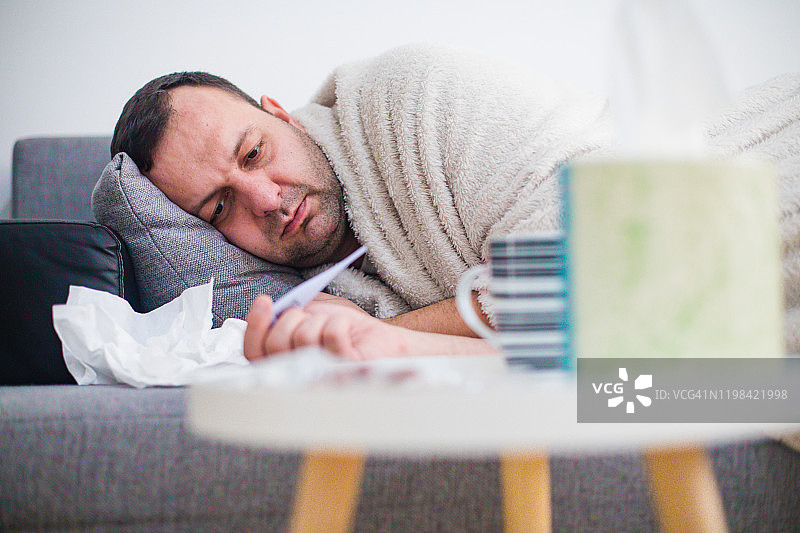 生病的男人在床上用体温计检查体温图片素材