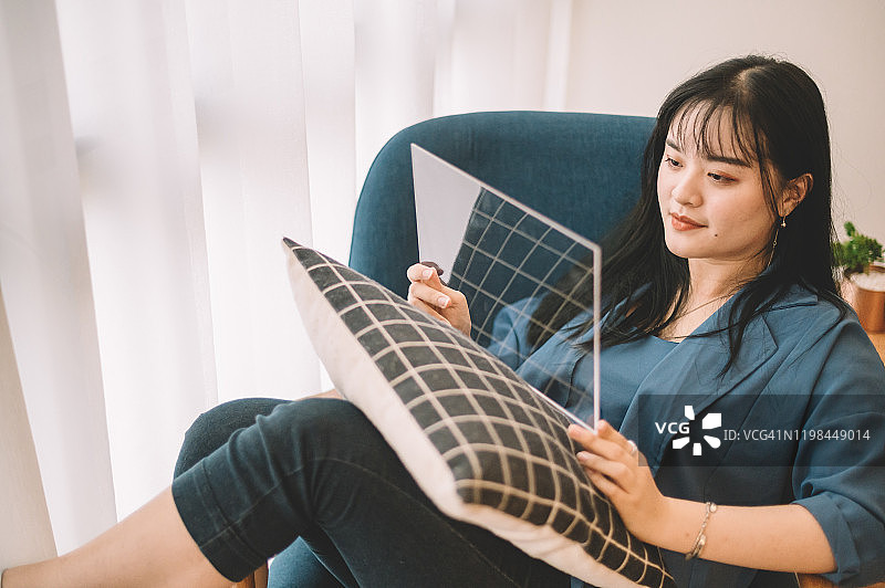 中国女性在客厅沙发上用透明平板电脑阅读医疗报告图片素材