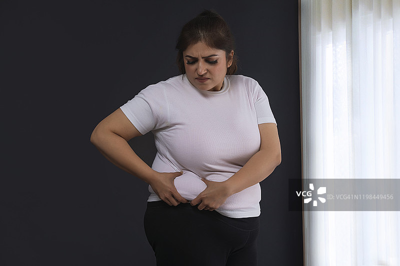 肥胖女人双手捂着肚子，面露震惊图片素材
