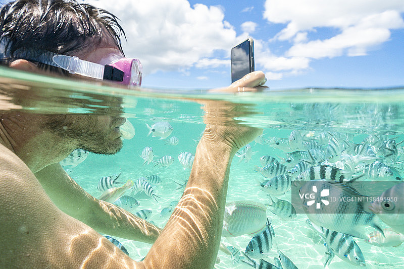 男人在毛里求斯印度洋用防水智能手机拍摄热带鱼图片素材