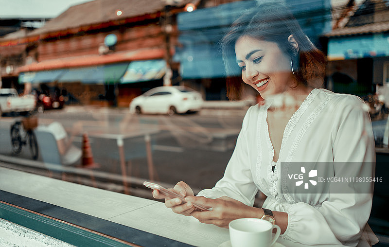 年轻女人坐在咖啡店的木桌旁，女商人喝着咖啡使用智能手机，手持电话并看屏幕，生活方式，科技概念图片素材