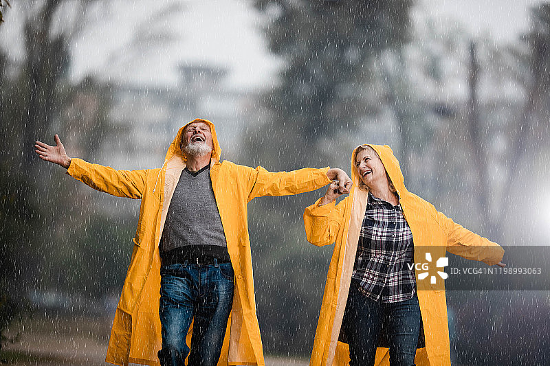 穿着雨衣的快乐中年夫妇在雨天公园里玩乐图片素材