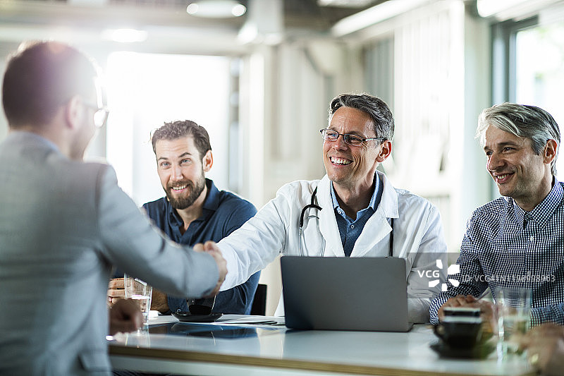 快乐的医生在办公室会议中与商人握手图片素材