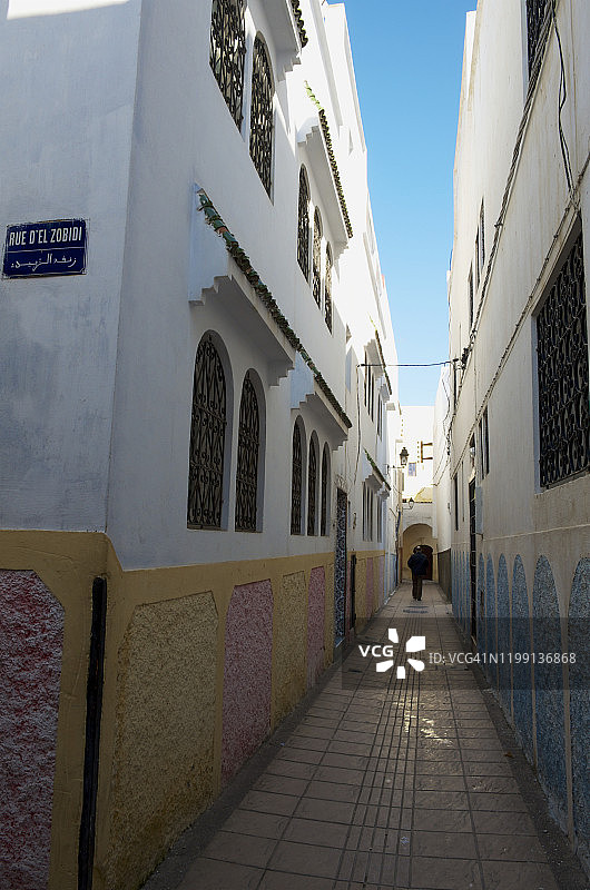 男人走在拉巴特麦地那的粉刷房屋之间的小巷里图片素材