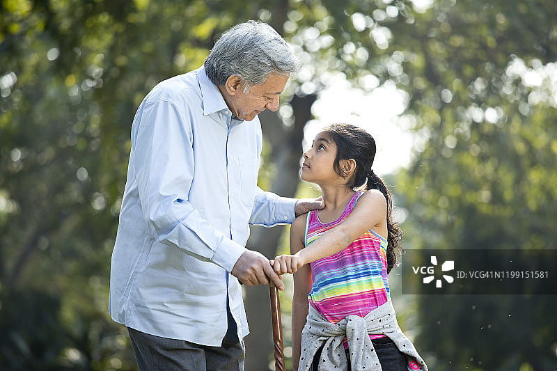 快乐的女孩在公园里牵着祖父的手图片素材