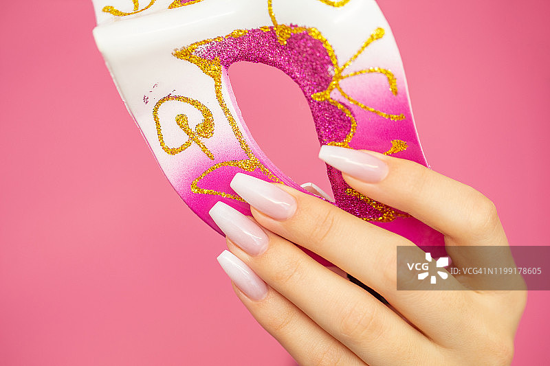 女人手持威尼斯面具，粉色背景图片素材