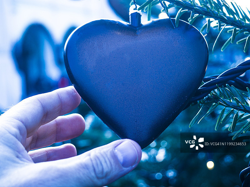 男人手靠近悬挂在松树上的心形装饰品图片素材
